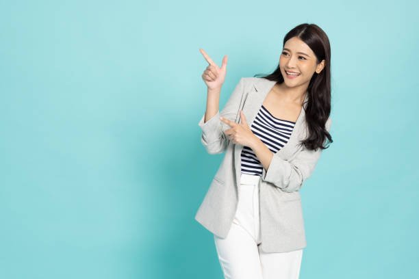 Young beautiful Asian business woman pointing to empty copy space isolated on green background